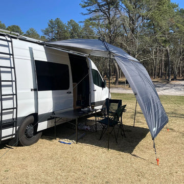 White van with a gray awning extended outdoors on a sunny day.