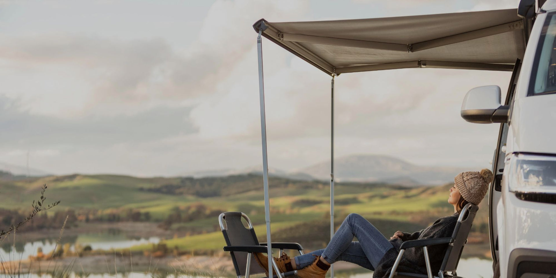 Person sitting under a canopy by a van with a scenic landscape in the background